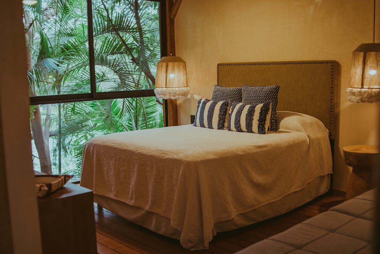 bedroom with warm tone covers on bed and palm trees outside